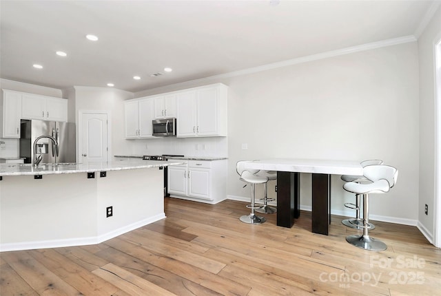 kitchen with a breakfast bar, light stone counters, appliances with stainless steel finishes, white cabinets, and backsplash