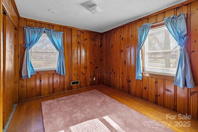 empty room with hardwood / wood-style flooring, wooden walls, and a textured ceiling