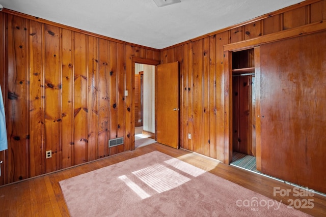 unfurnished bedroom featuring wooden walls, a closet, and light wood-type flooring