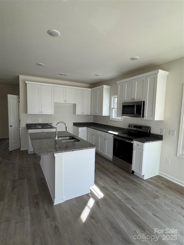 kitchen with appliances with stainless steel finishes, white cabinetry, an island with sink, sink, and hardwood / wood-style flooring