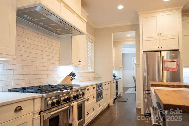 kitchen with premium range hood, high quality appliances, white cabinets, wooden counters, and ornamental molding