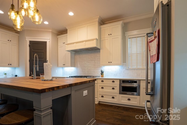 kitchen with appliances with stainless steel finishes, wood counters, decorative light fixtures, white cabinetry, and ornamental molding