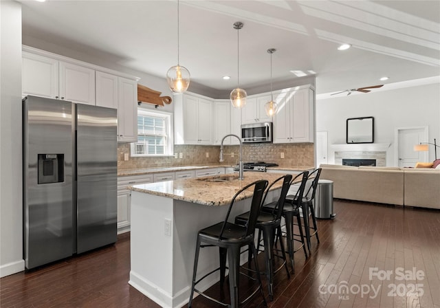 kitchen with a breakfast bar, sink, white cabinets, light stone counters, and stainless steel appliances