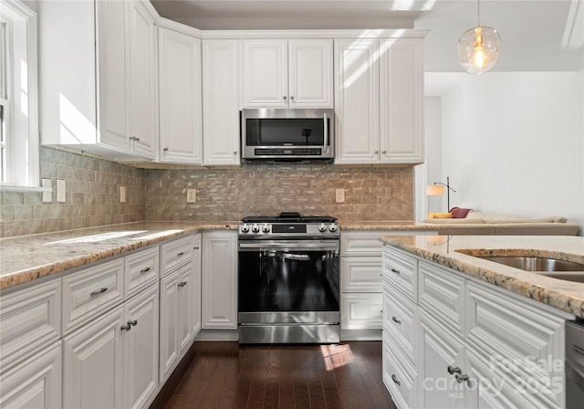 kitchen featuring pendant lighting, white cabinetry, light stone counters, stainless steel appliances, and dark wood-type flooring