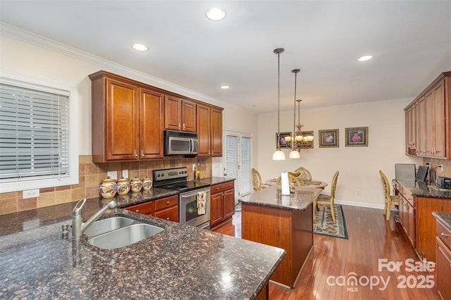 kitchen with pendant lighting, sink, appliances with stainless steel finishes, a kitchen island with sink, and dark stone counters