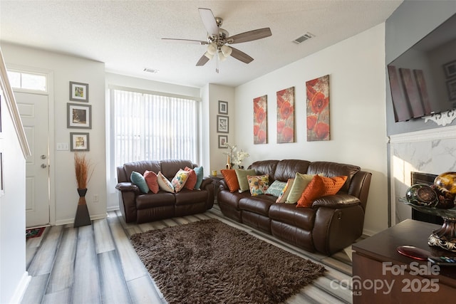 living room with hardwood / wood-style flooring, ceiling fan, a high end fireplace, and a textured ceiling