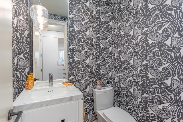 half bath with vanity, toilet, and wallpapered walls