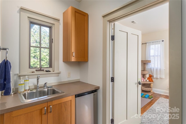 kitchen with dishwashing machine, wood finished floors, a sink, visible vents, and baseboards