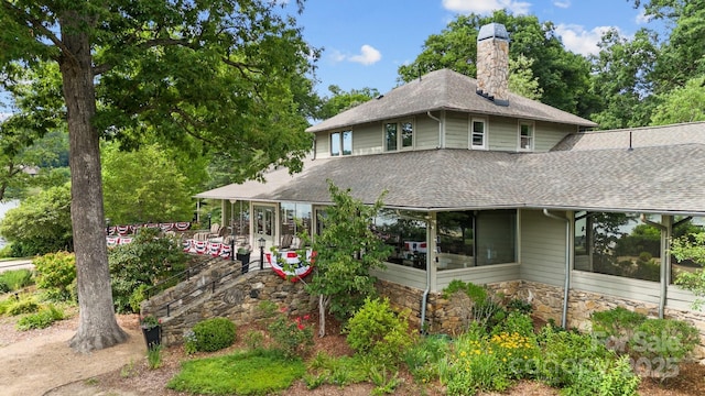 exterior space with stone siding, a shingled roof, and a chimney