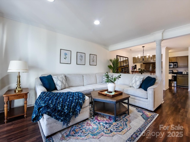 living room featuring ornate columns, ornamental molding, dark wood-type flooring, and a notable chandelier