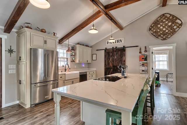 kitchen with a kitchen bar, light stone counters, black appliances, a barn door, and cream cabinetry