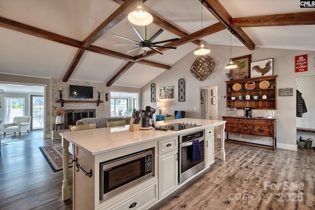 kitchen featuring a breakfast bar, white cabinetry, stainless steel appliances, a center island, and a brick fireplace