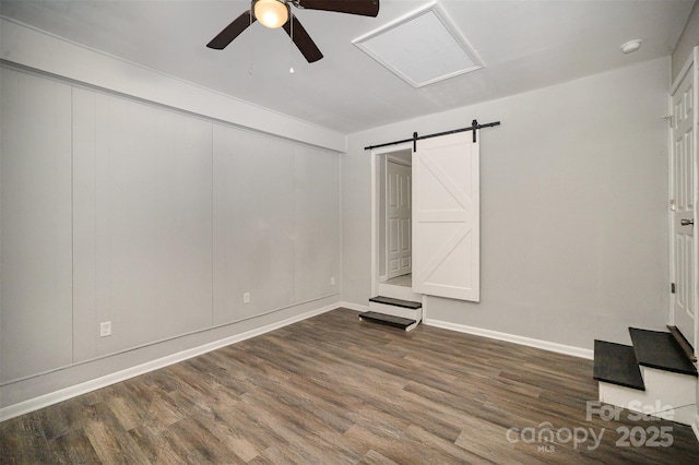 spare room featuring dark wood-type flooring, a barn door, and ceiling fan