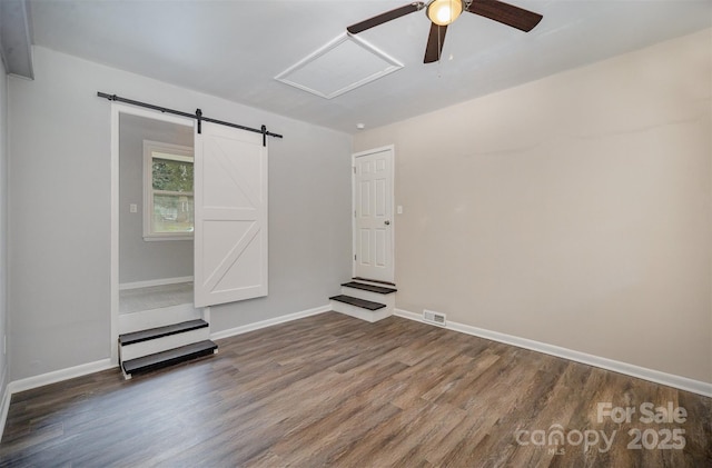 spare room featuring dark wood-type flooring, a barn door, and ceiling fan