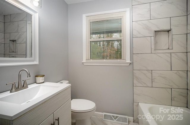 full bathroom featuring vanity, tiled shower / bath, and toilet