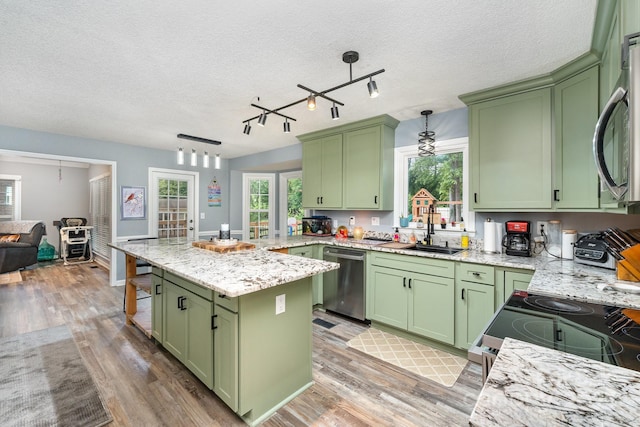 kitchen with green cabinets, appliances with stainless steel finishes, a sink, light wood-type flooring, and a textured ceiling