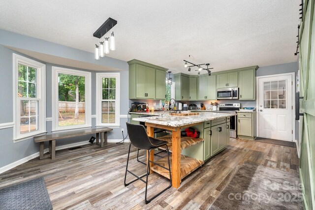 kitchen featuring green cabinets, stainless steel appliances, wood finished floors, a textured ceiling, and baseboards