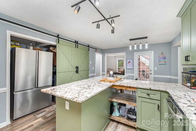 kitchen with green cabinets, stainless steel appliances, light wood-style floors, a textured ceiling, and a barn door