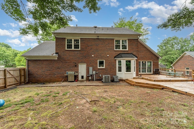 rear view of house with brick siding, a deck, fence, cooling unit, and roof with shingles