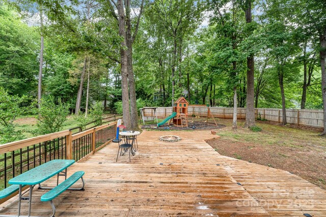 wooden terrace with a playground, a fenced backyard, and view of scattered trees