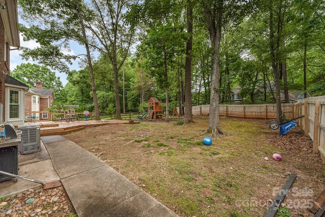 fenced backyard with a playground, a deck, and view of scattered trees