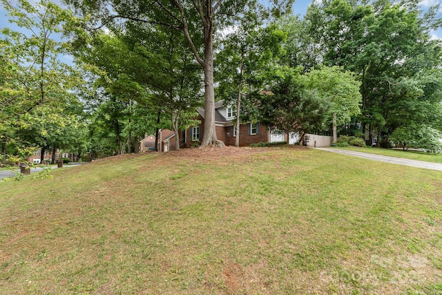 view of front facade featuring brick siding, a front yard, driveway, and view of scattered trees
