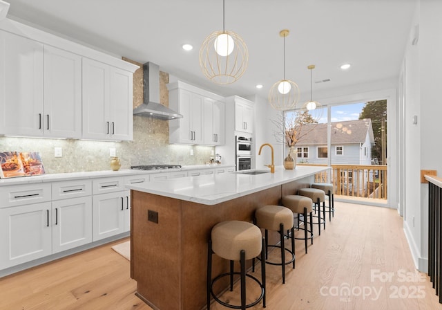 kitchen with white cabinetry, pendant lighting, wall chimney exhaust hood, and a center island with sink