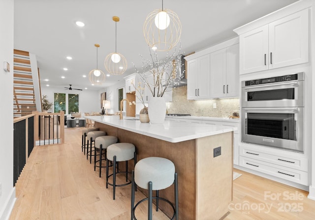 kitchen featuring decorative light fixtures, white cabinets, a kitchen breakfast bar, stainless steel double oven, and a spacious island