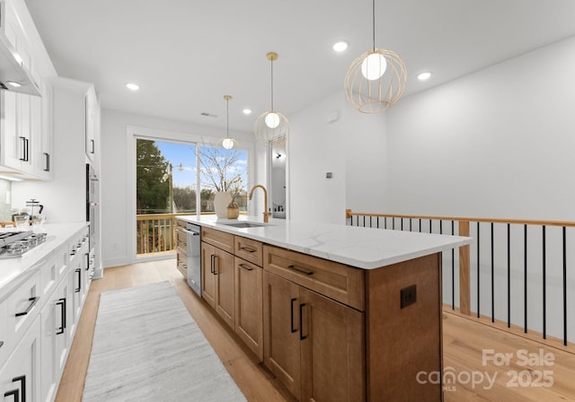 kitchen featuring white cabinetry, sink, an island with sink, and wall chimney exhaust hood