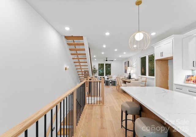 kitchen with light stone counters, a kitchen breakfast bar, pendant lighting, light hardwood / wood-style floors, and white cabinets