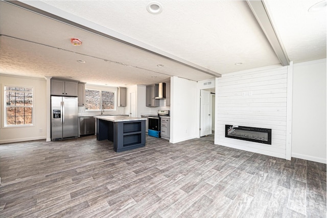 kitchen with a kitchen island, appliances with stainless steel finishes, a large fireplace, beam ceiling, and wall chimney exhaust hood