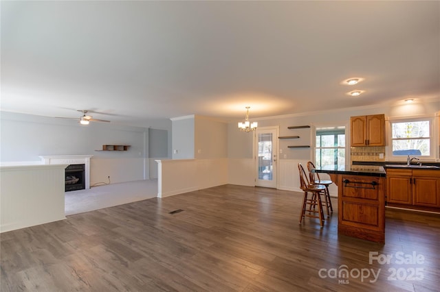 kitchen featuring dark countertops, dark wood-style floors, ceiling fan with notable chandelier, and a kitchen breakfast bar