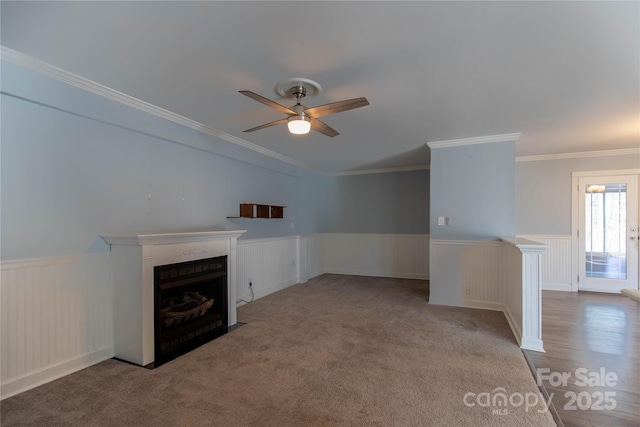 unfurnished living room with a fireplace with flush hearth, a ceiling fan, wainscoting, and crown molding