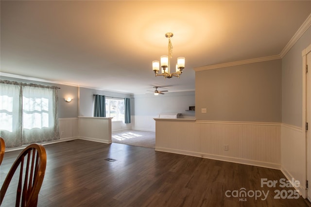 unfurnished dining area with visible vents, dark wood-type flooring, wainscoting, crown molding, and ceiling fan with notable chandelier