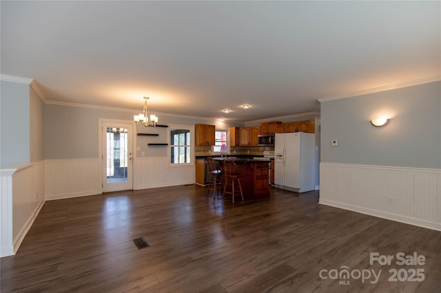 unfurnished living room with a chandelier, visible vents, wainscoting, and dark wood finished floors