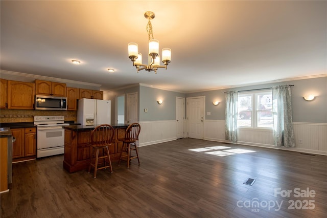 kitchen featuring dark countertops, a center island, white appliances, wainscoting, and a chandelier