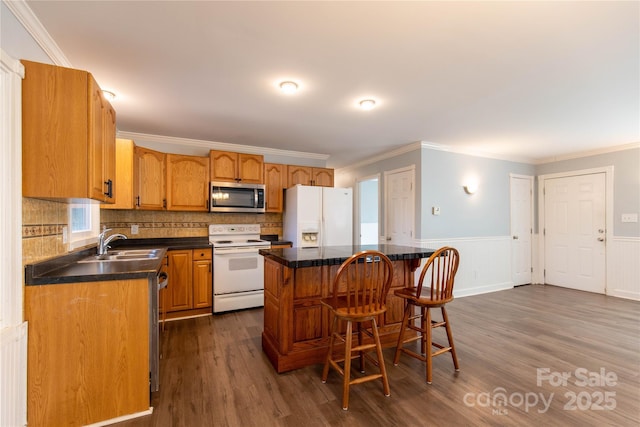 kitchen with white appliances, a sink, wainscoting, a kitchen breakfast bar, and a center island