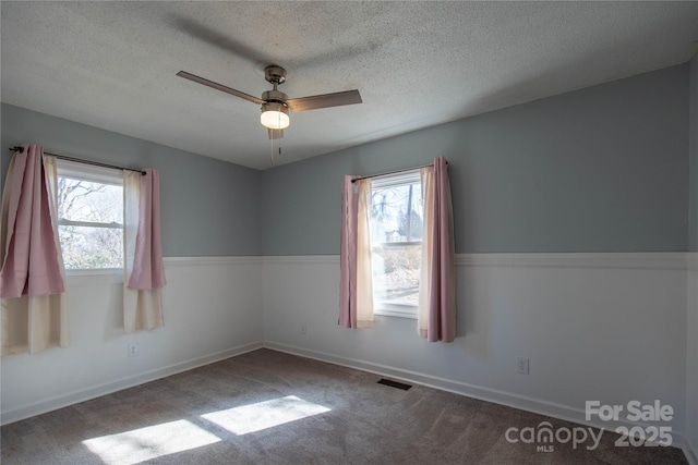 empty room with plenty of natural light, visible vents, carpet floors, and ceiling fan