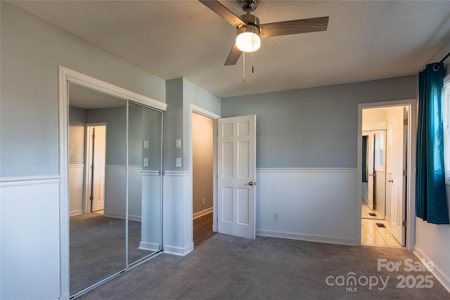 unfurnished bedroom featuring ceiling fan, dark colored carpet, connected bathroom, a textured ceiling, and a closet