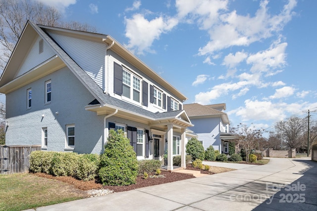 view of front of house with a shingled roof, concrete driveway, and fence