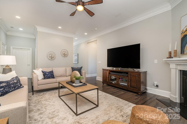 living area featuring ceiling fan, a fireplace, wood finished floors, baseboards, and crown molding