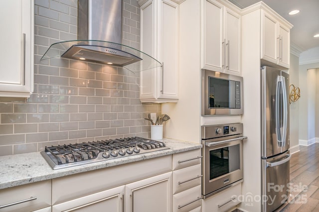 kitchen with baseboards, appliances with stainless steel finishes, wood finished floors, wall chimney range hood, and backsplash