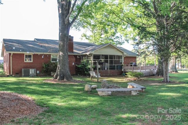 rear view of property featuring a sunroom, brick siding, a wooden deck, and a lawn