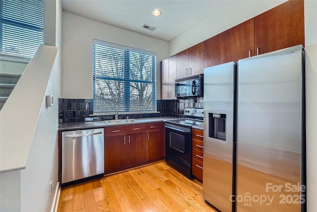 kitchen with light wood-type flooring, sink, decorative backsplash, and black appliances