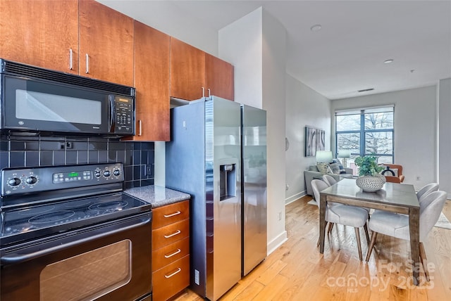 kitchen with light hardwood / wood-style flooring, decorative backsplash, and black appliances