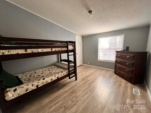 bedroom featuring vaulted ceiling, crown molding, a textured ceiling, and light wood-type flooring