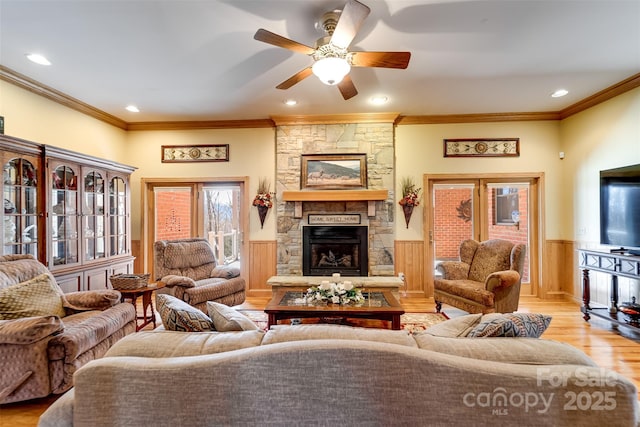 living room featuring crown molding, a stone fireplace, light hardwood / wood-style flooring, and ceiling fan