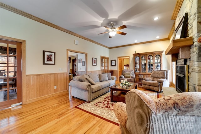 living room with ceiling fan, a stone fireplace, crown molding, and light hardwood / wood-style floors