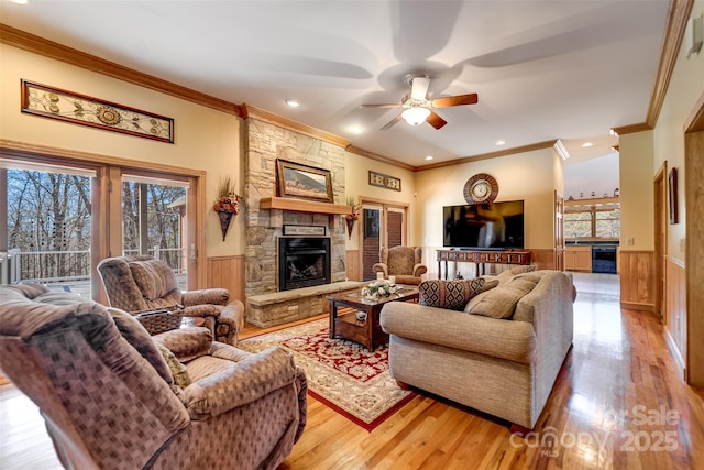 living room featuring crown molding, ceiling fan, a stone fireplace, and light wood-type flooring