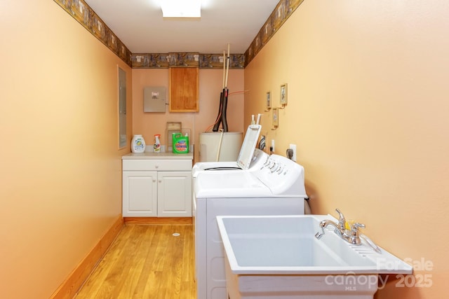 washroom with water heater, sink, cabinets, washing machine and dryer, and light hardwood / wood-style flooring